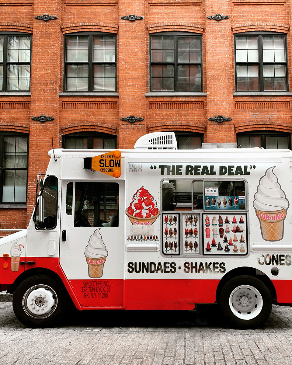 Un camion de glace blanc et rouge, décoré avec des cônes de glace, stationne dans une rue à New York.